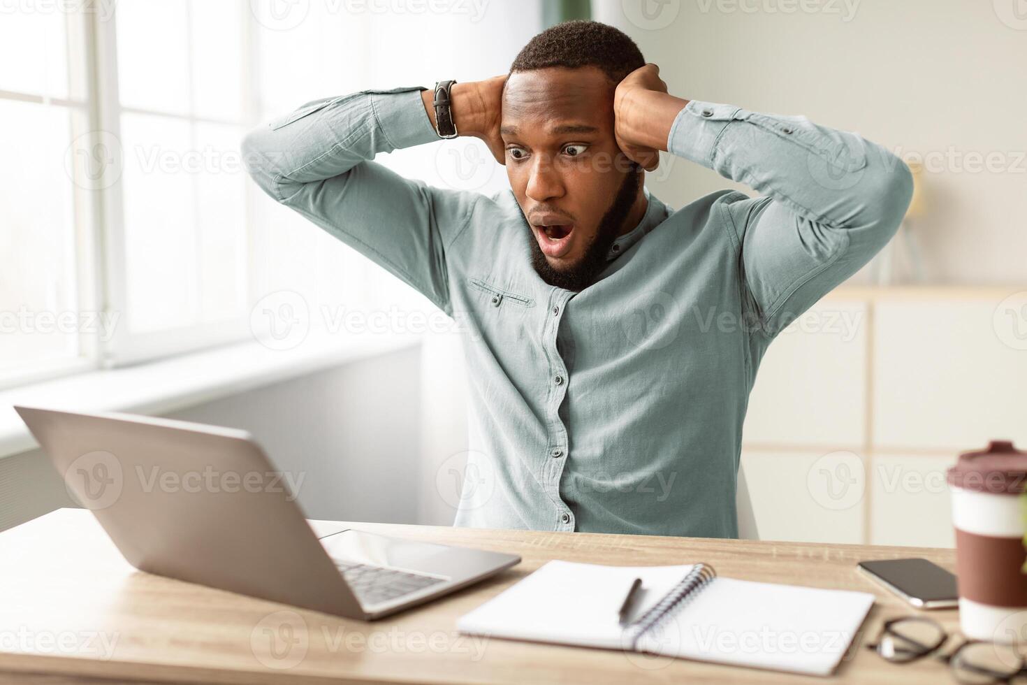 Oops, Problem At Workplace. Shocked African Businessman Looking At Laptop Computer Having Issue Working Online Sitting In Modern Office. Internet Connection Error Concept. Selective Focus photo