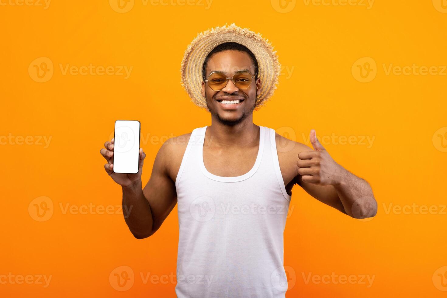 Check out this new mobile application. Happy African American guy showing cellphone with mockup for website or app, gesturing thumb up on yellow studio background photo