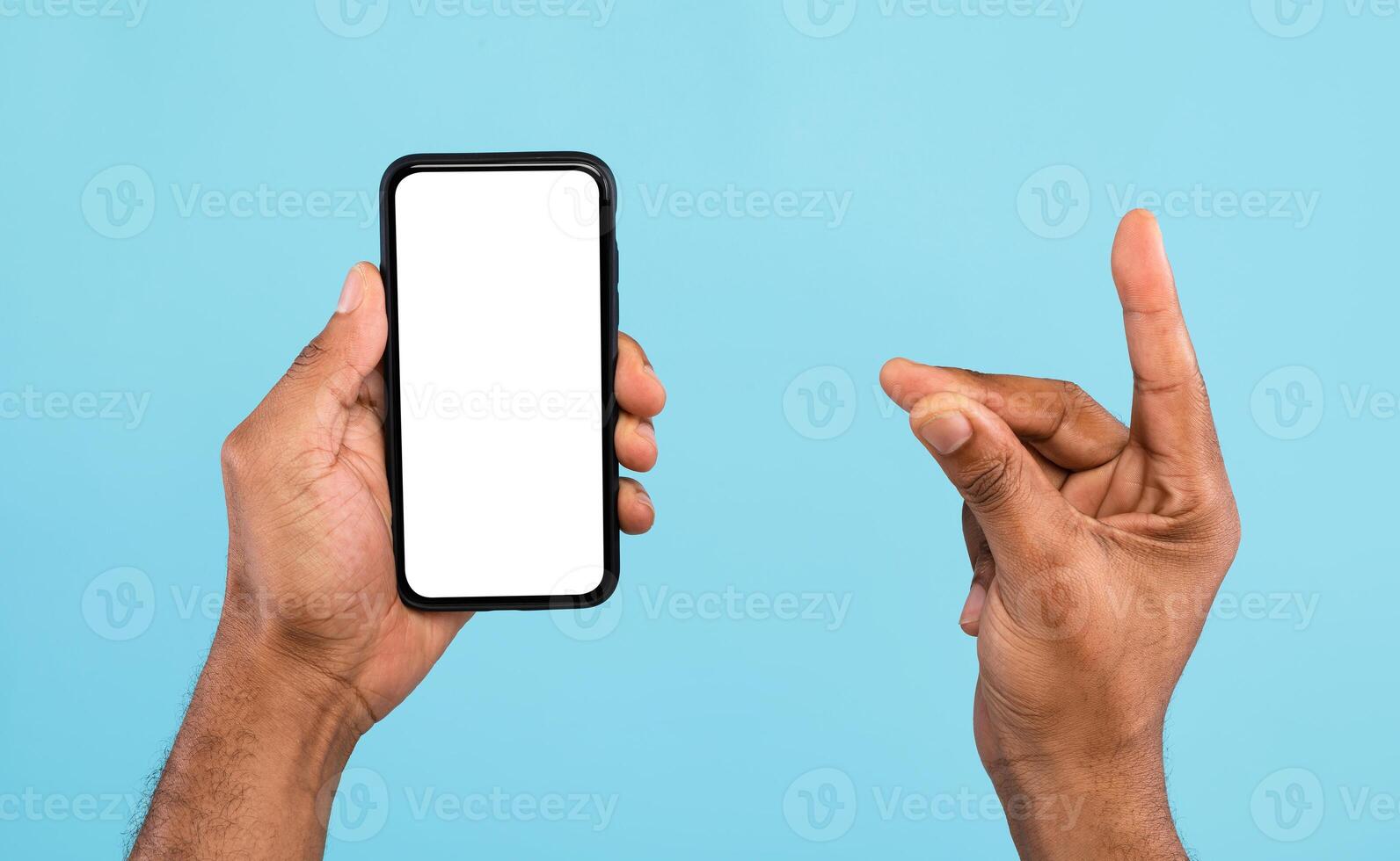 Cropped view of young black guy showing smartphone with empty white screen and holding something on blue background, mockup for mobile app, website and business card design photo