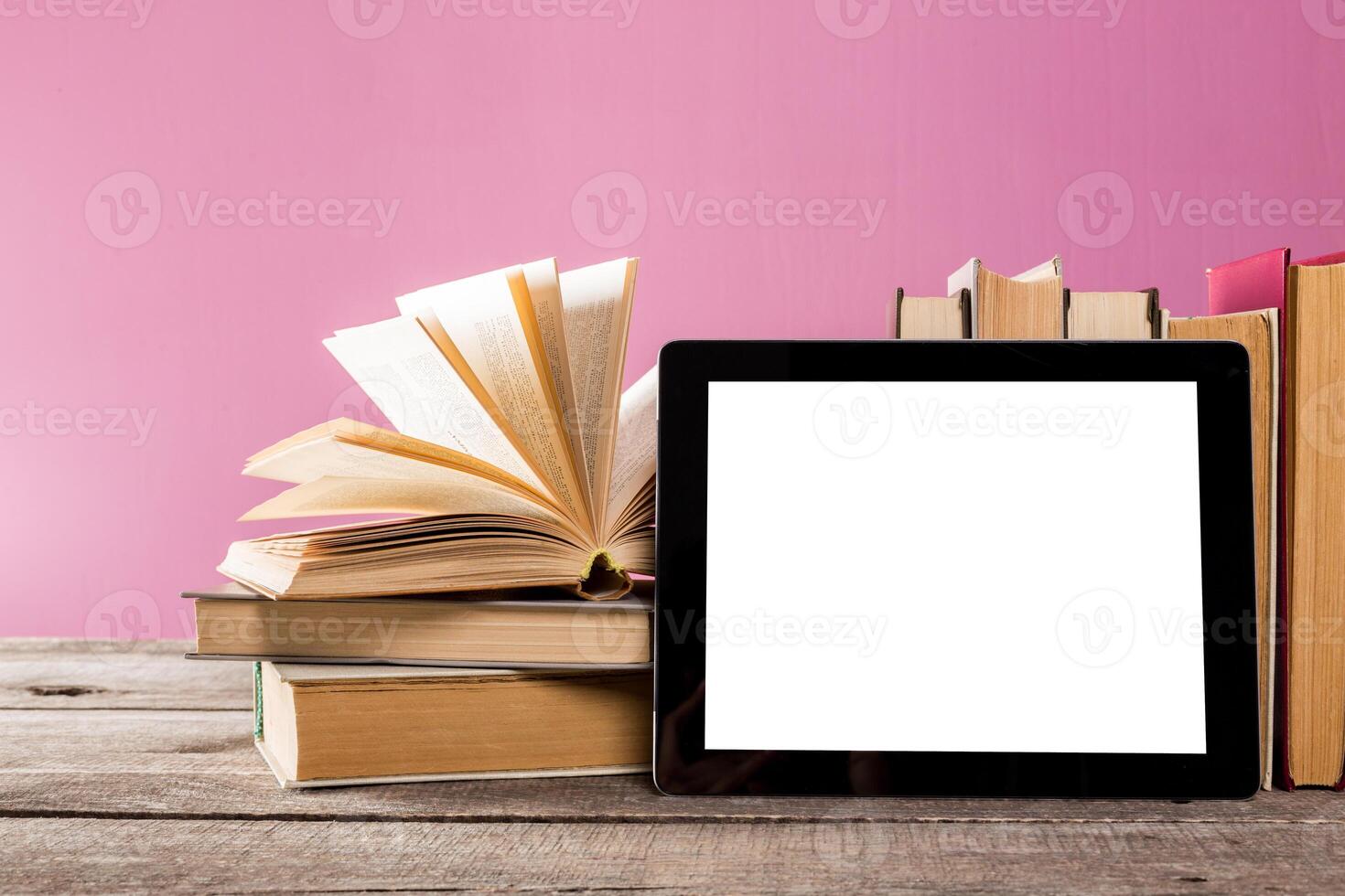Modern reading setup with books and a tablet on a wooden table with a pink background photo