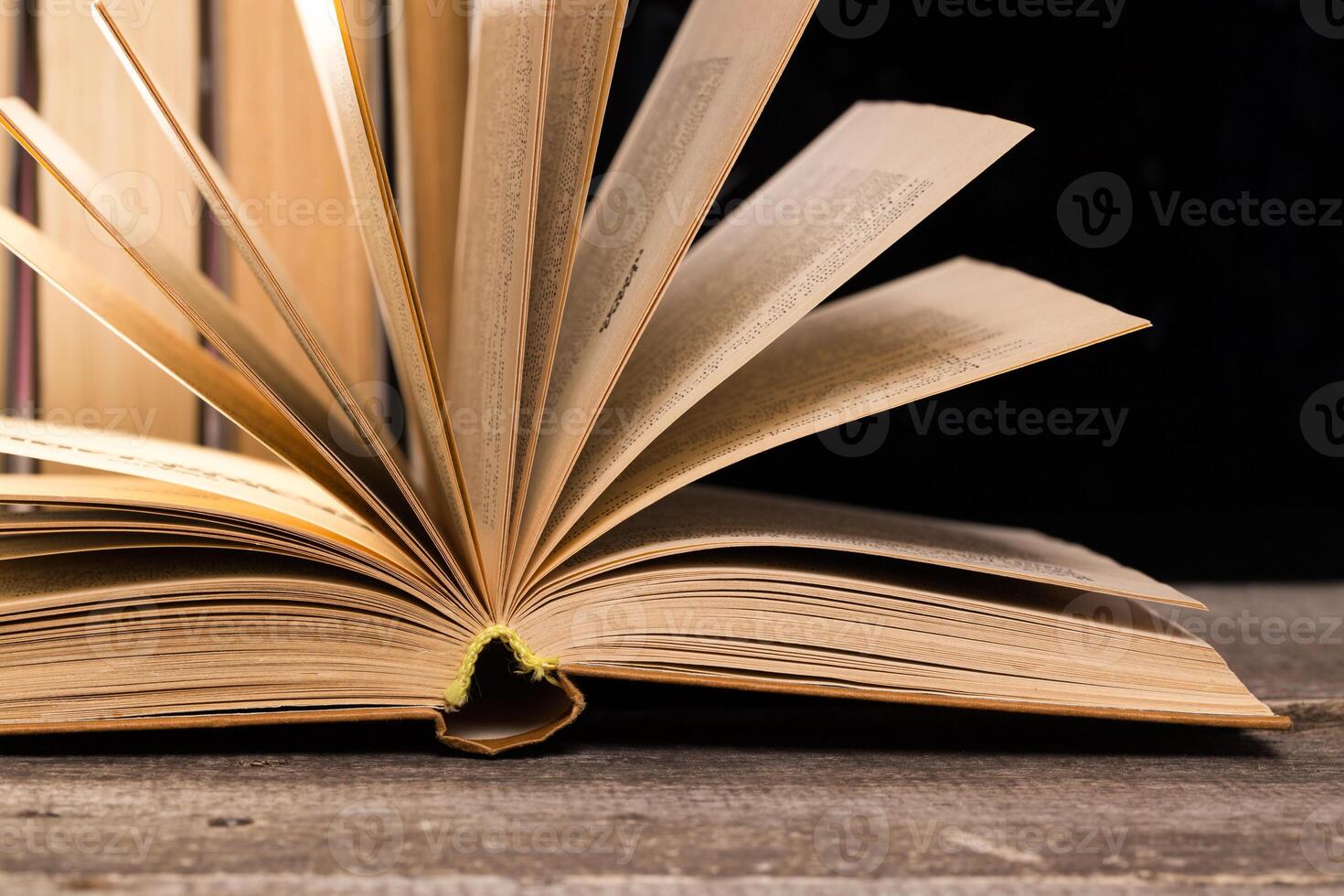 Open book resting on wooden table with pages fanned out towards the viewer in dim light photo