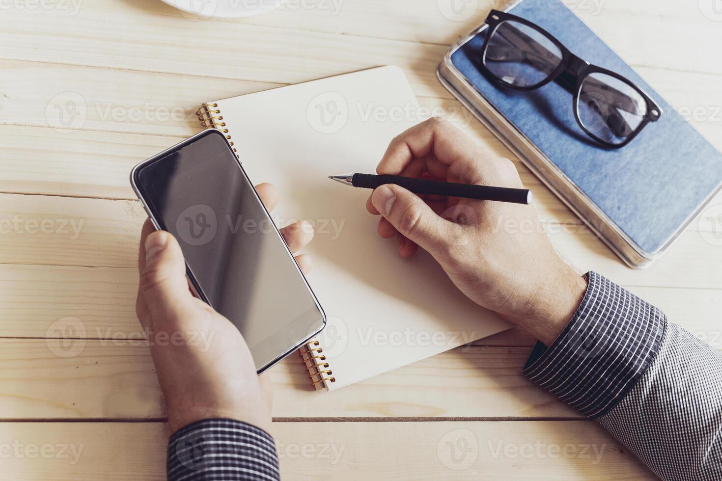 Writing notes while using a smartphone in a cozy workspace during the afternoon photo
