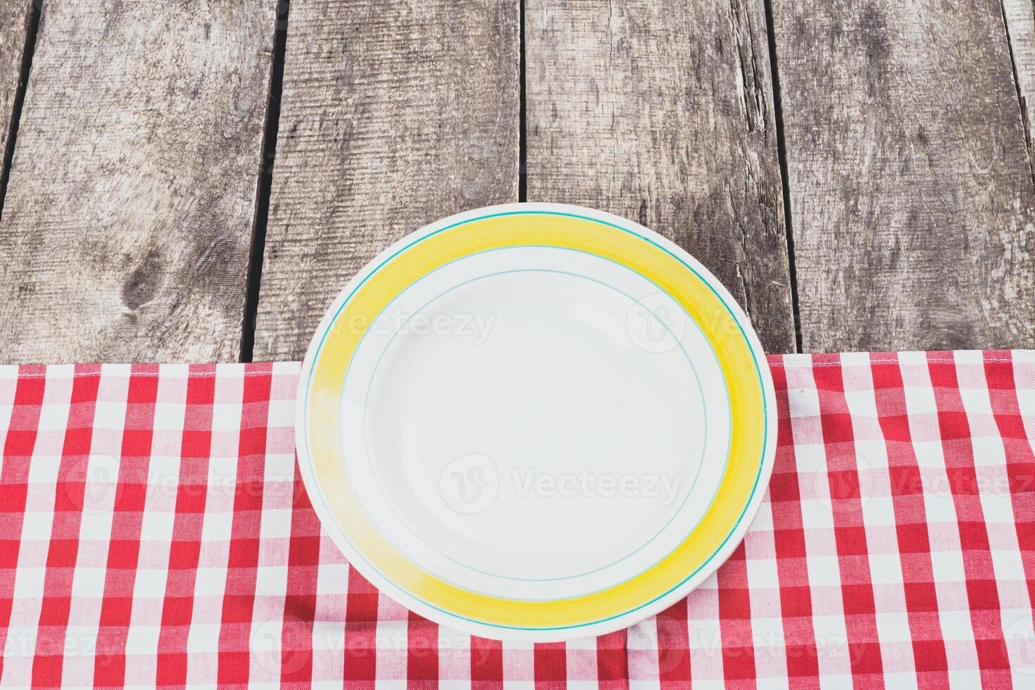 Empty plate on a red checkered tablecloth in a rustic setting during daytime photo