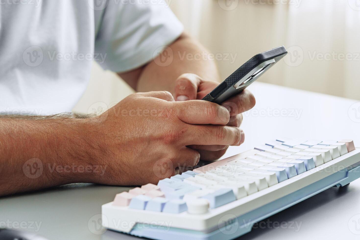 Person using smartphone while sitting at desk with mechanical keyboard in modern workspace photo