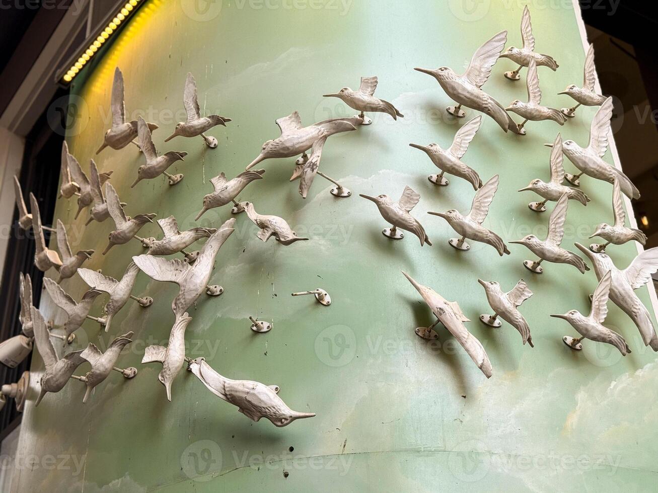 White bird sculptures attached to a green wall creating an impression of flock in flight. Symbolism of freedom, motion, and collective unity represented in design. photo
