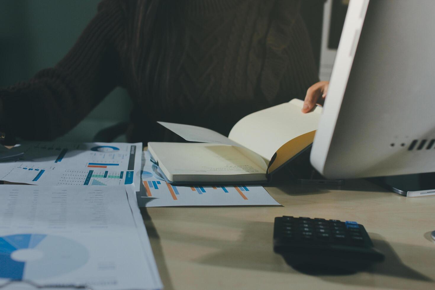A person is working on a computer with a notebook and papers photo