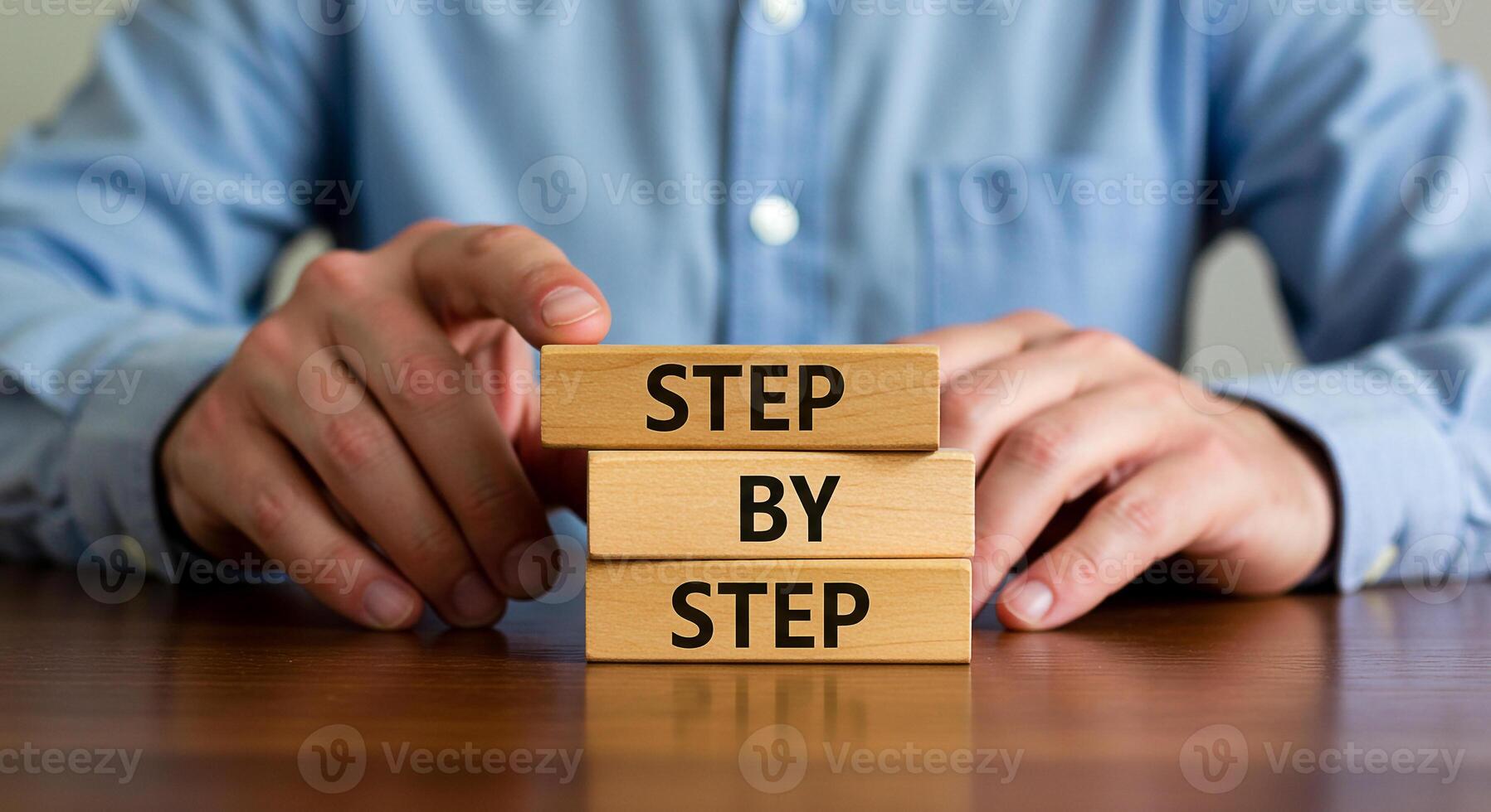 Man arranging wooden blocks with the words Step by Step on a desk demonstrating a process plan or strategy The image evokes concepts of growth progress and careful planning in a business or profession photo