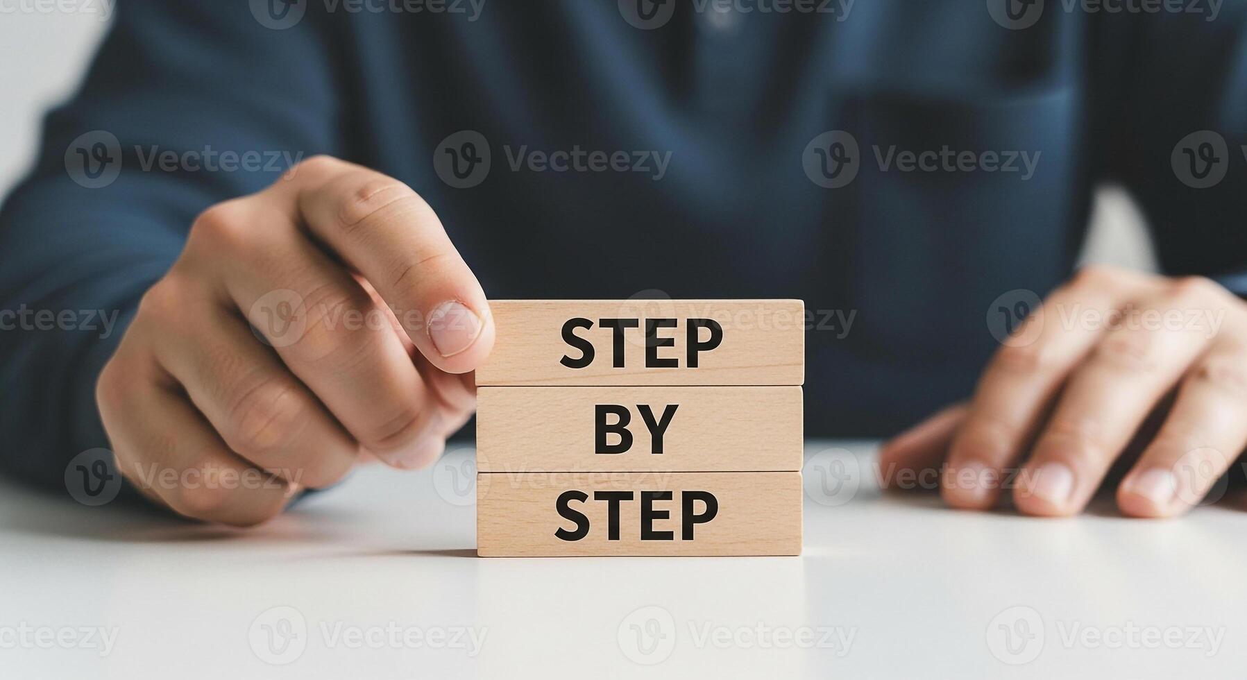 Close-up of male hands arranging wooden blocks spelling out Step by Step on a white table, signifying a process, guidance, or a methodical approach to problem-solving The image evokes feelings of plan photo