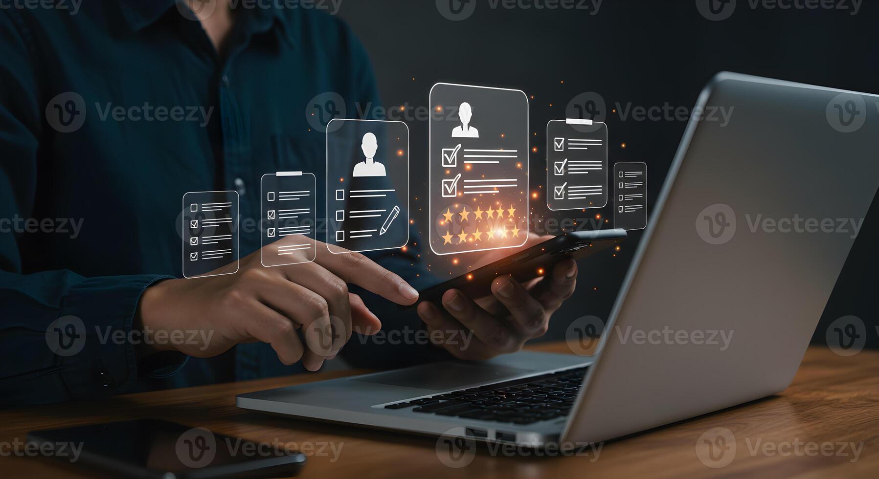Person reviewing applications using a smartphone and laptop evaluating resumes and candidate profiles with a checklist and star rating in a modern office setting The image depicts a thorough and metic photo