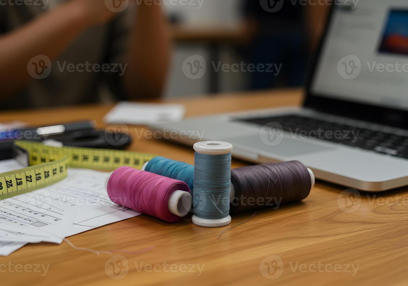Spools of colorful threads arranged on a wooden desk next to a laptop symbolizing the modern fashion design process and the blend of technology and craftsmanship photo
