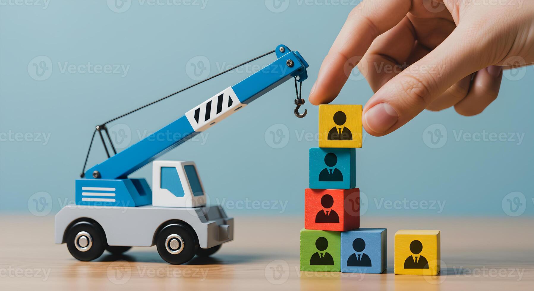Hand placing wooden block with person icon on stack using toy crane conceptual image for human resources teamwork and business growth strategy The colorful blocks represent a diverse team signifying c photo