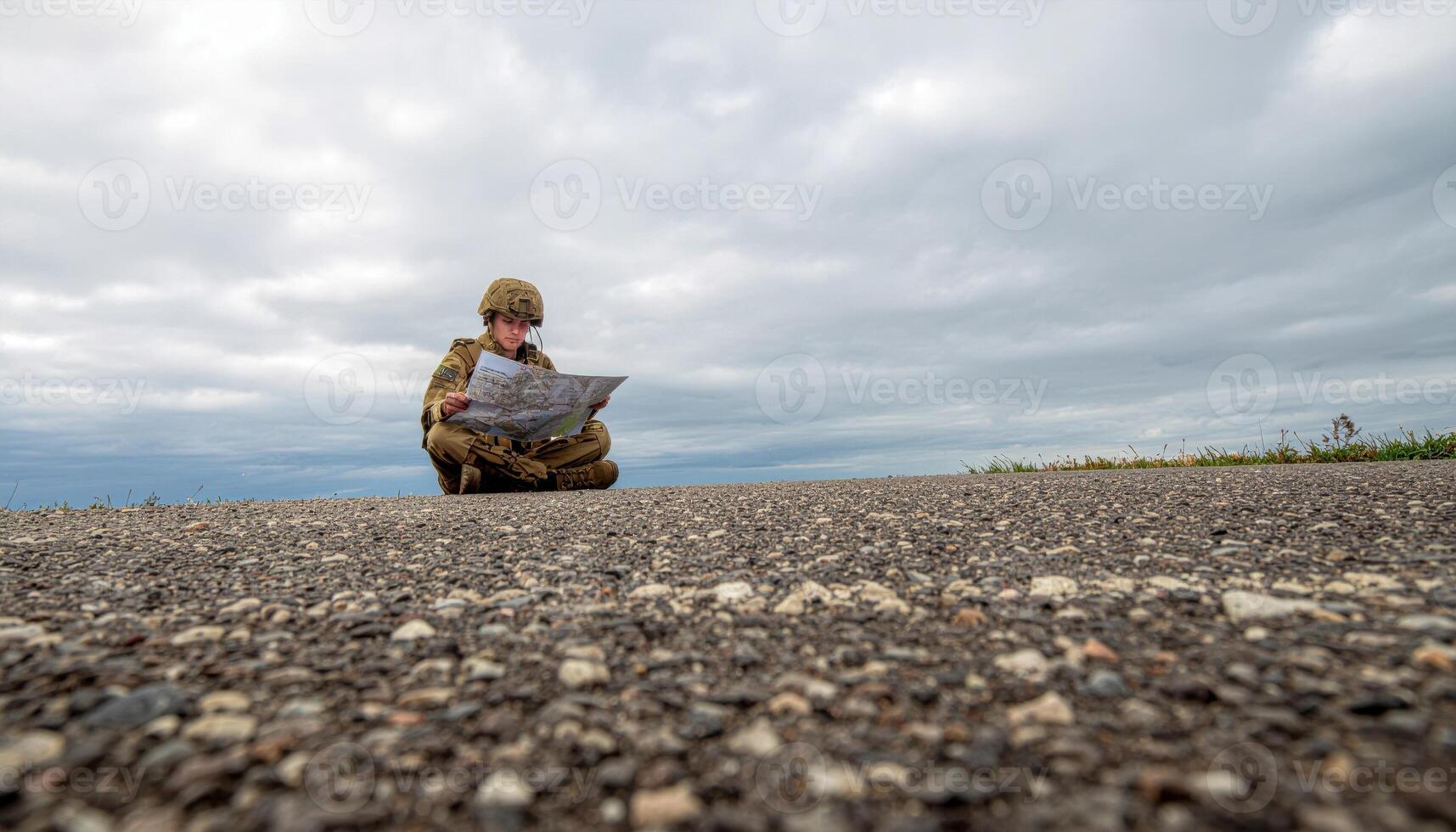 Fictional soldier reading paper map under overcast sky gentle top light neutral gear with covered badges wide negative space field navigation and planning concept photo