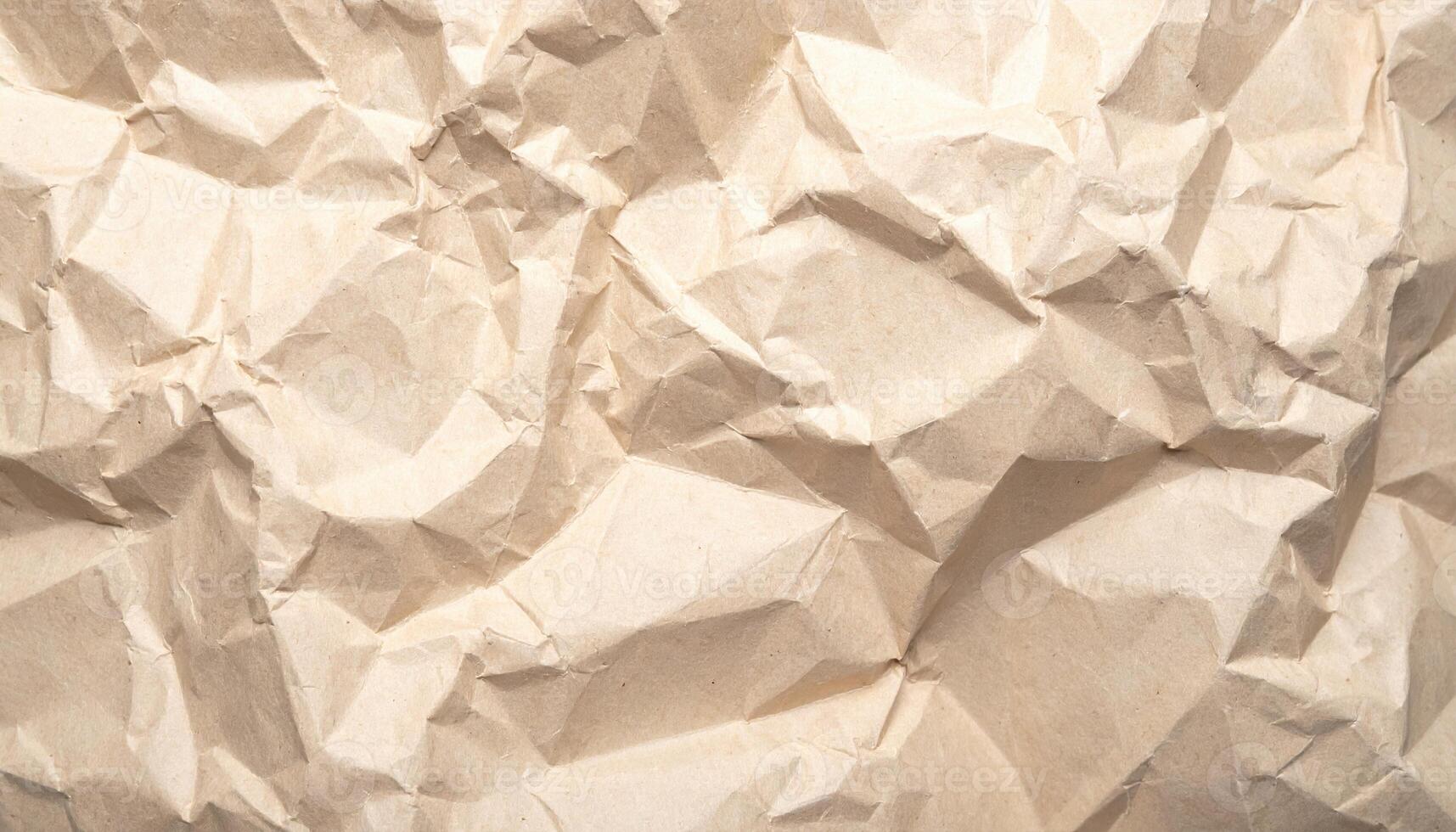 The full frame view showcases a textured surface of crumpled brown paper, creating an abstract pattern with highlights and shadows across its rugged terrain. photo