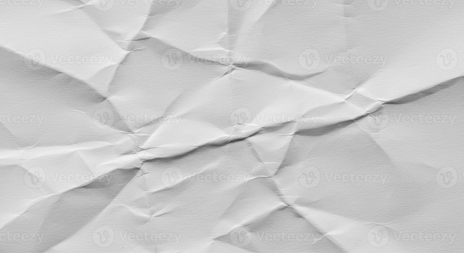 The close-up photograph shows a crumpled and wrinkled white sheet of paper creating an abstract texture with varying shades of light and shadow. photo