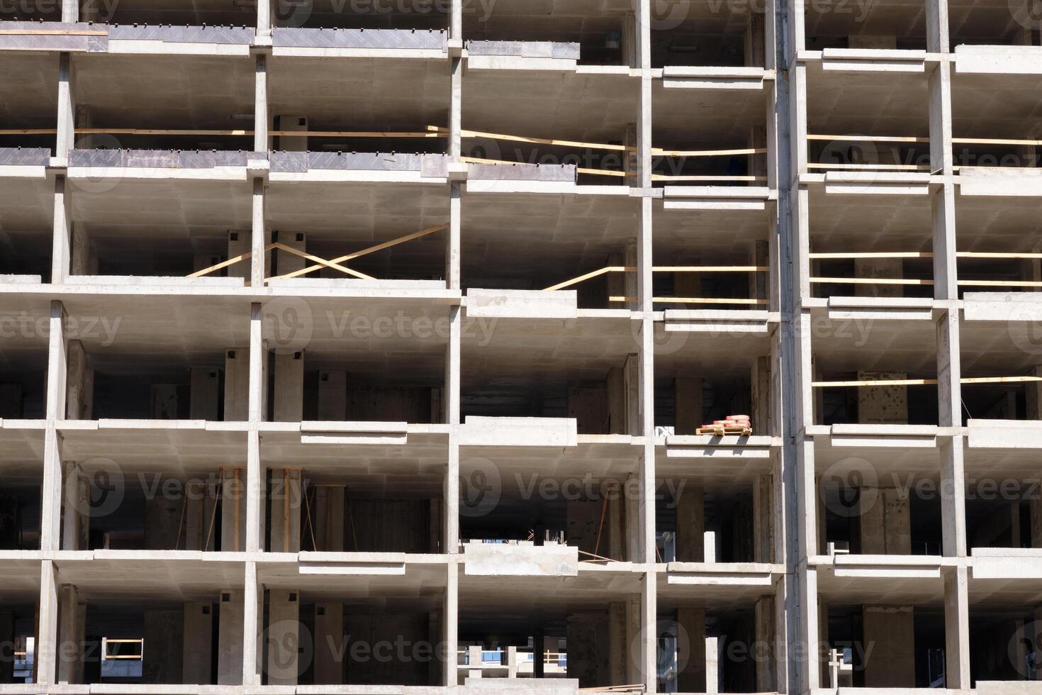 A tall multi story building is being constructed with open concrete floors and wooden supports, illuminated by sunlight. The structure awaits further development photo