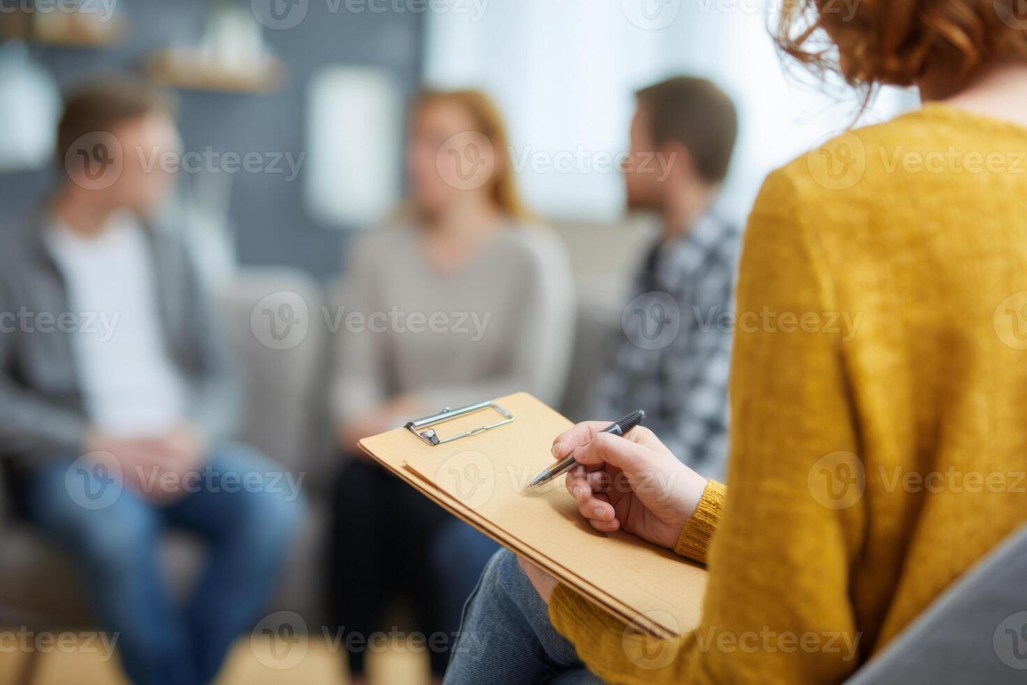 A counselor takes notes while observing a group therapy session. Three participants engage in a thoughtful conversation, contributing to a supportive atmosphere photo