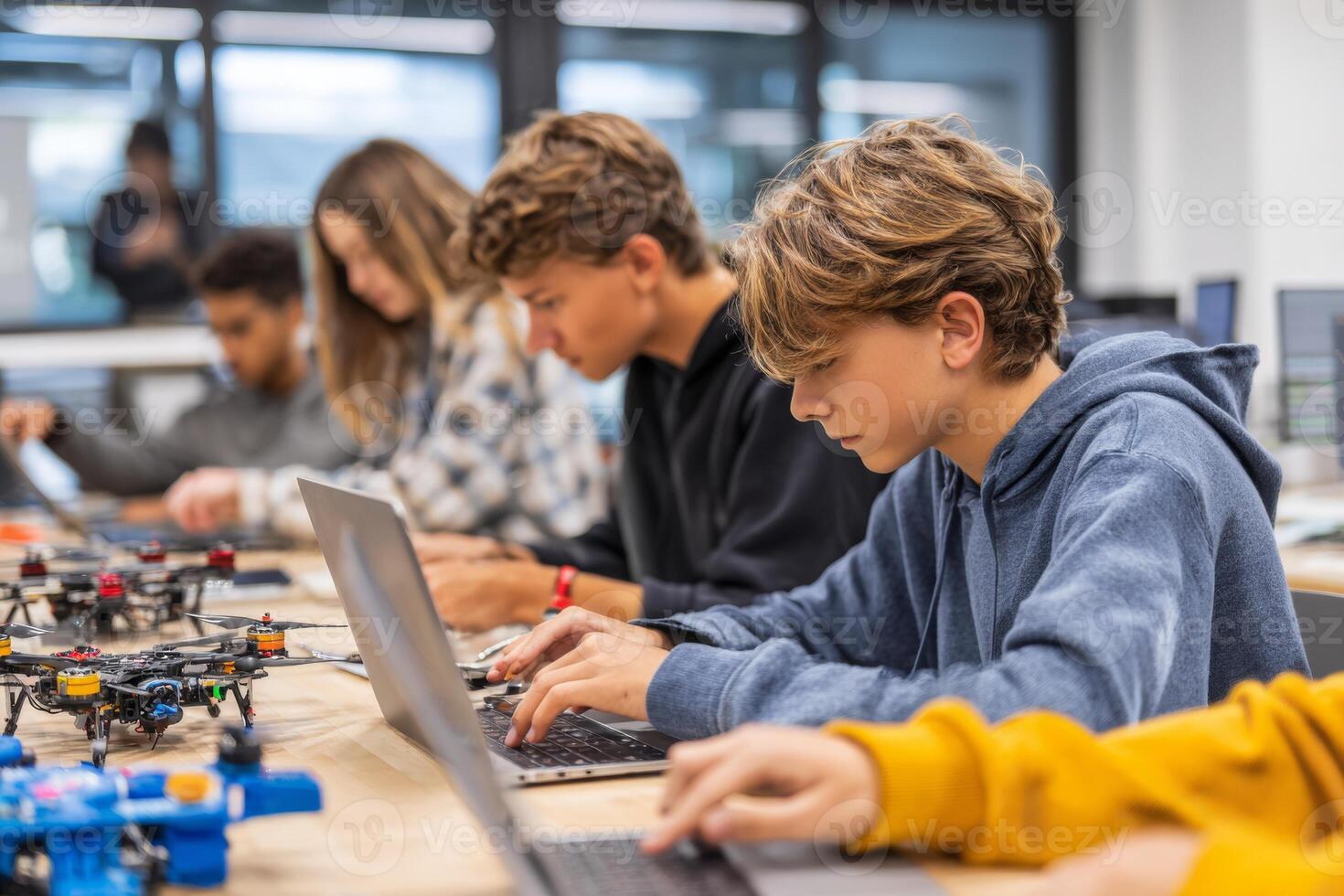 Young learners are actively participating in a technology workshop. They are coding and assembling drones while seated at desks equipped with laptops. The environment is collaborative and innovative photo
