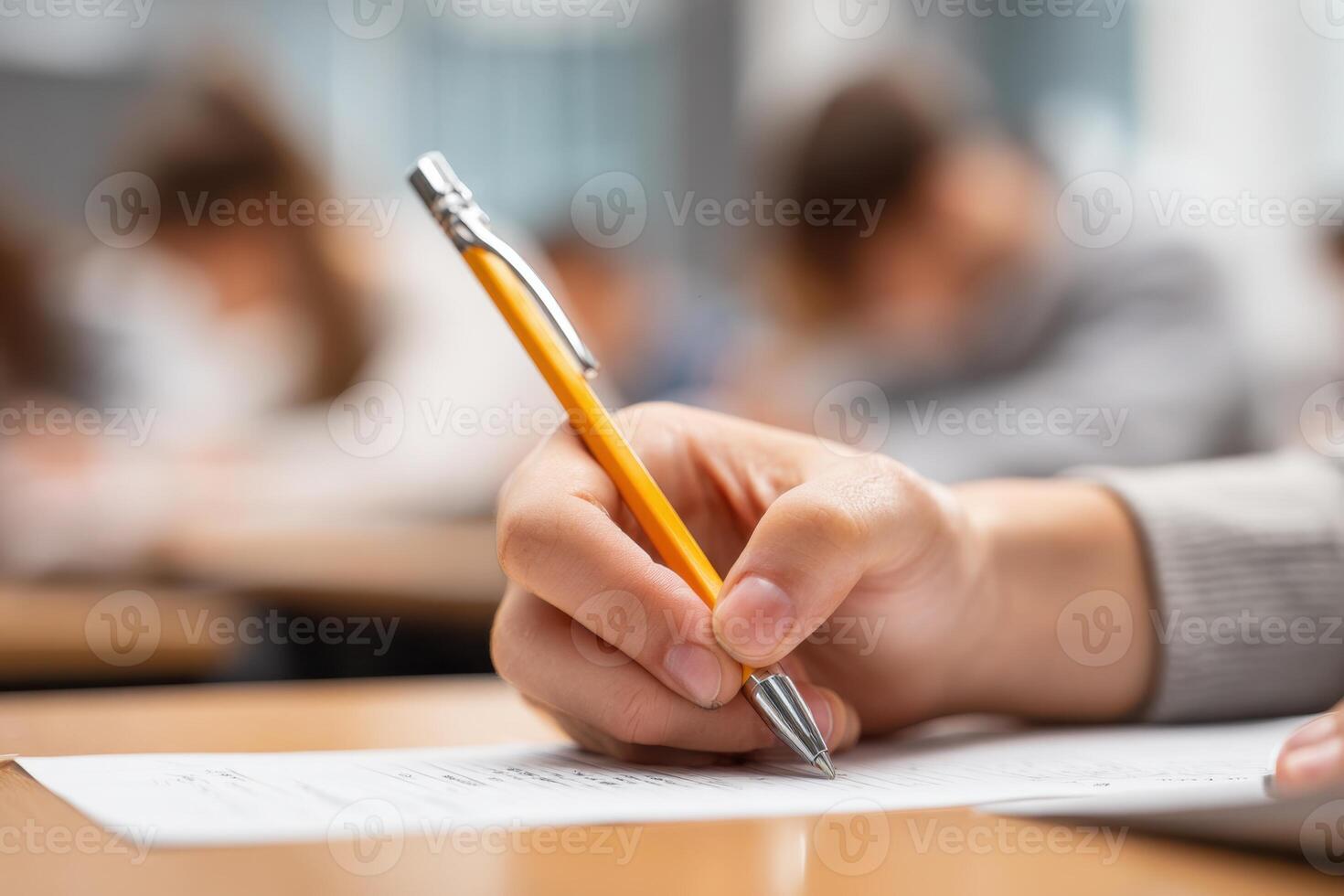 Close-up of a hand holding a pen and paper, doing an exam in school, writing something. Blurred background. The student is sitting at their desk, taking a mental test for a final-year class. photo