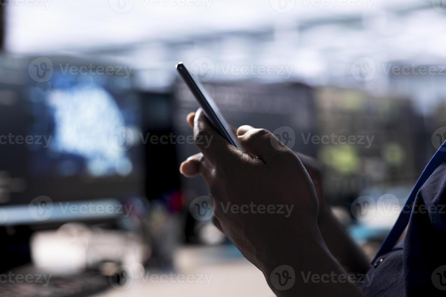 Data center worker passing time by texting friends on mobile phone in office, taking break from work. Close up shot of server hub employee checking social media feed on smartphone photo
