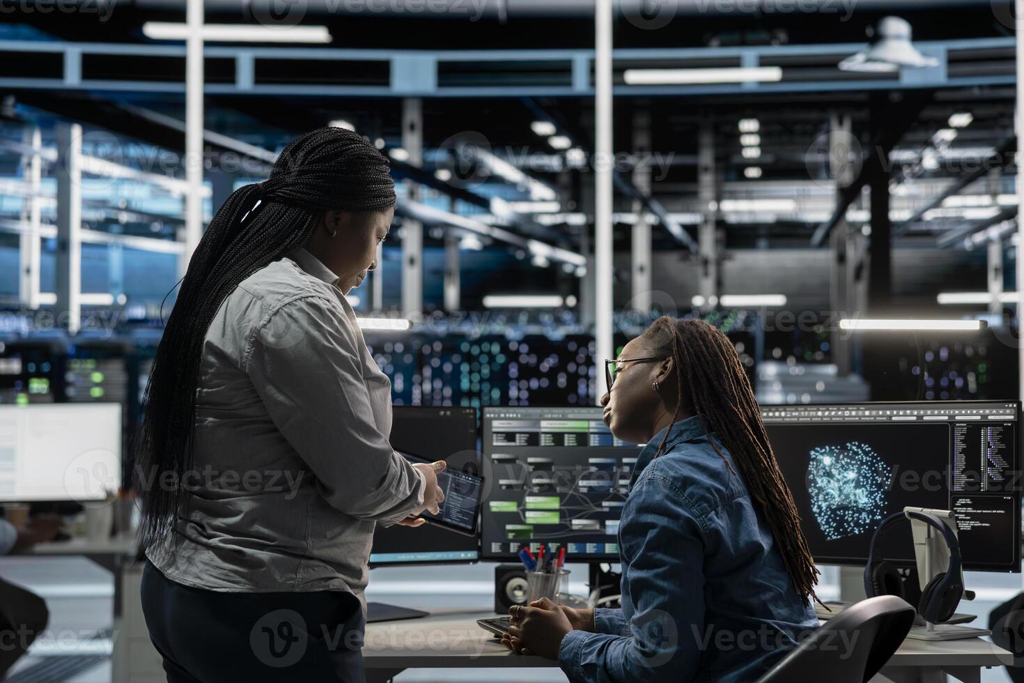 Data center engineers talking, doing brainstorming, using artificial intelligence visualization tools to identify errors. Server hub coworkers working together, looking at insights photo