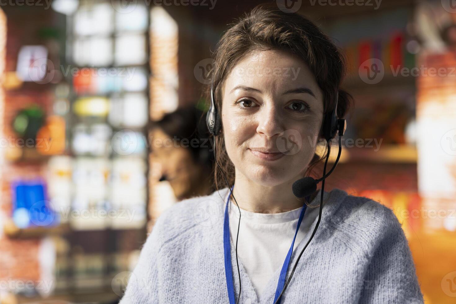 Portrait of cheerful call center employee in office helping customers by answering questions, solving their issue. Joyous customer support worker using headset mic to talk with clients photo