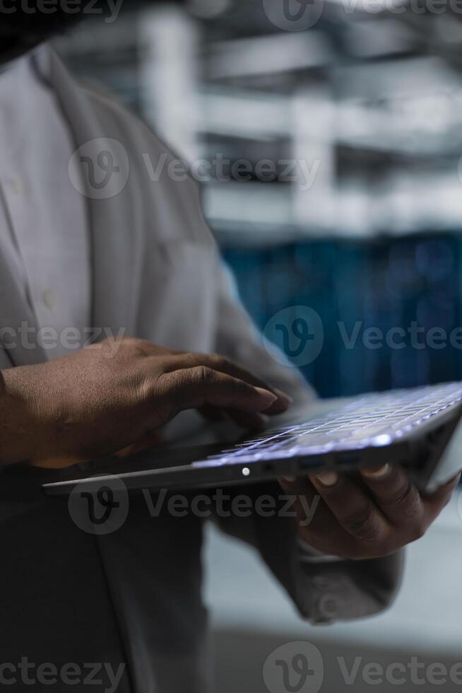 Close up of admin in data center typing on laptop keyboard, writing code, refining algorithms. Server hub IT specialist using programming scripts on laptop, doing resource optimization photo