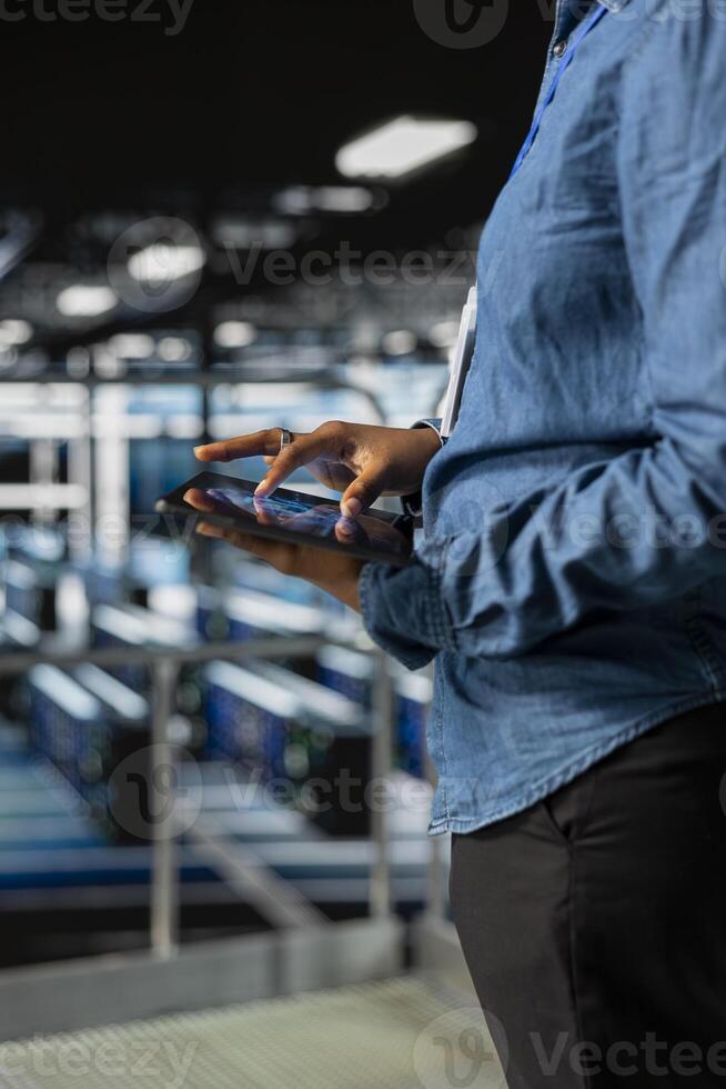 Close up of black admin using tablet to do infrastructure AI machine learning automatization in server farm, doing maintenance using neural network systems. Data center software developer. photo