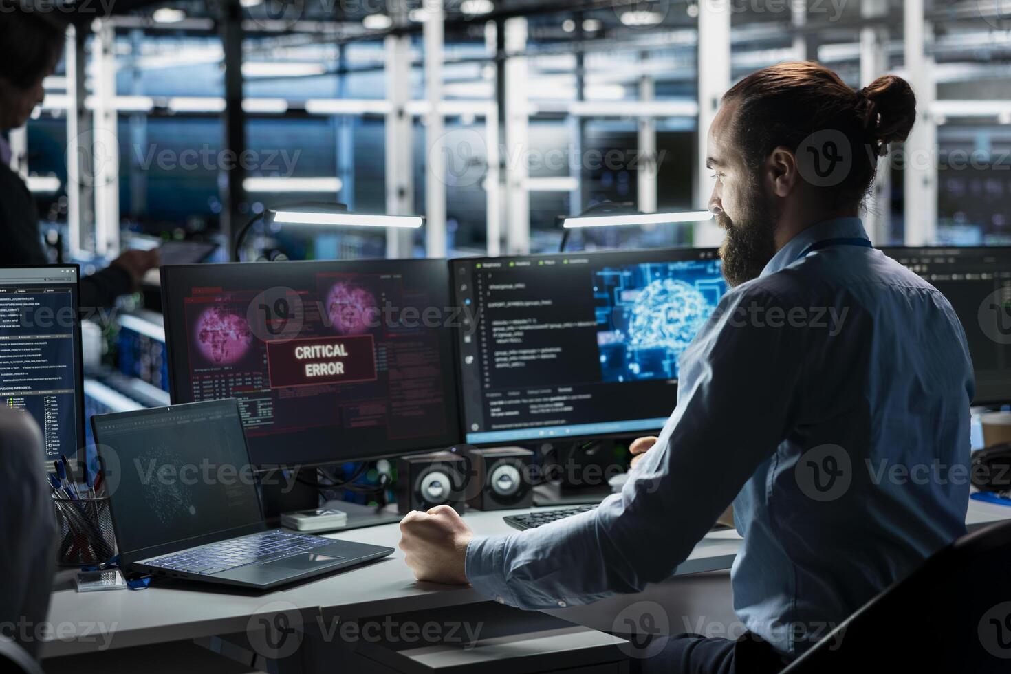 Frustrated data center system administrator at desk upset by malfunctioning gear while using AI. Upset server room IT worker disgruntled by errors in glitching artificial intelligence software photo