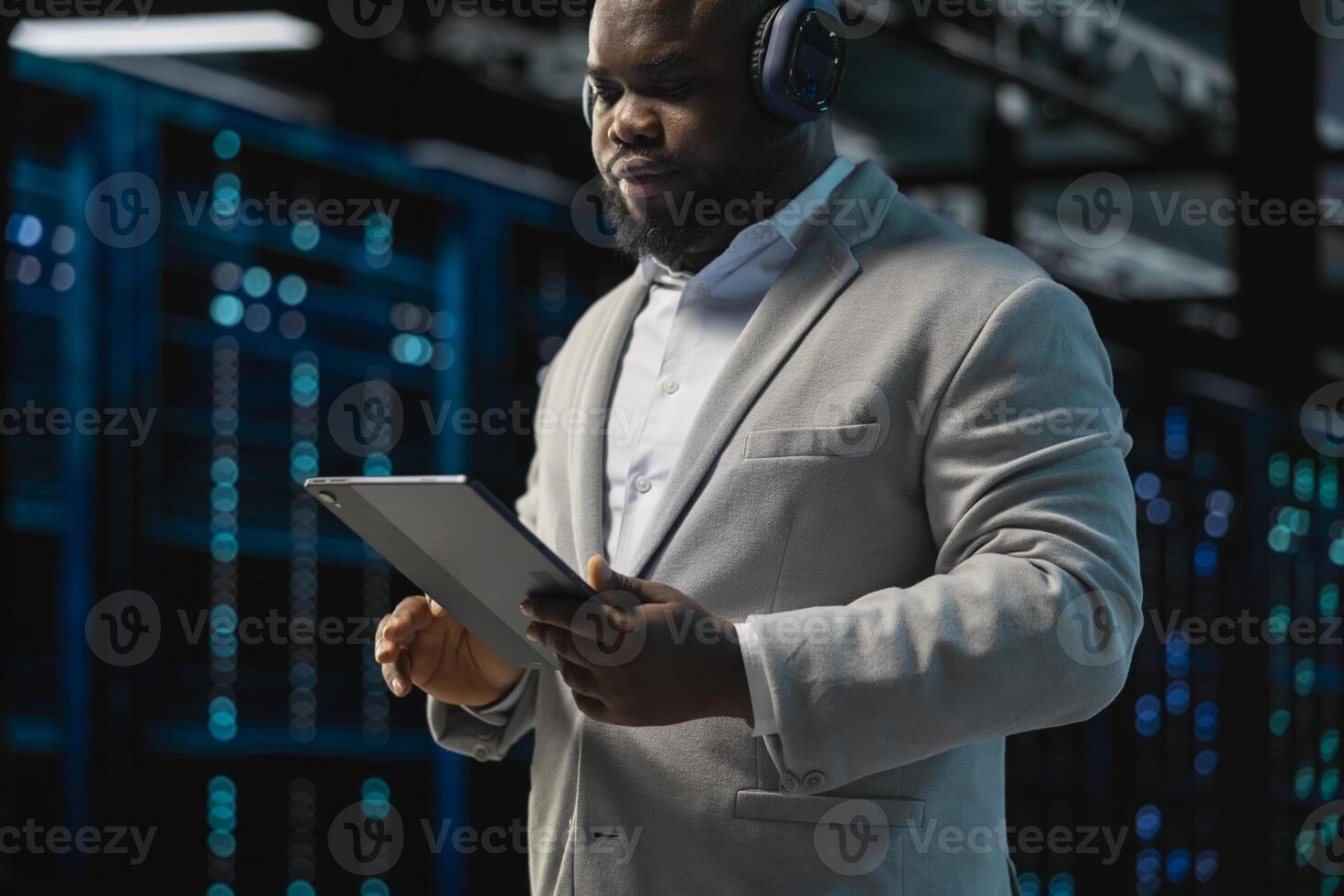 Server room IT expert listening music while fixing network issues affecting rigs performance. Data center programmer wearing audio headphones running system diagnostic tests on tablet photo