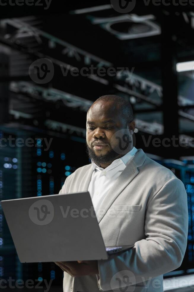 Server hub developer using laptop to fix network issues affecting storage arrays, doing backups. Programmer in data center runs system diagnostic tests, scanning hardware logs for faults photo