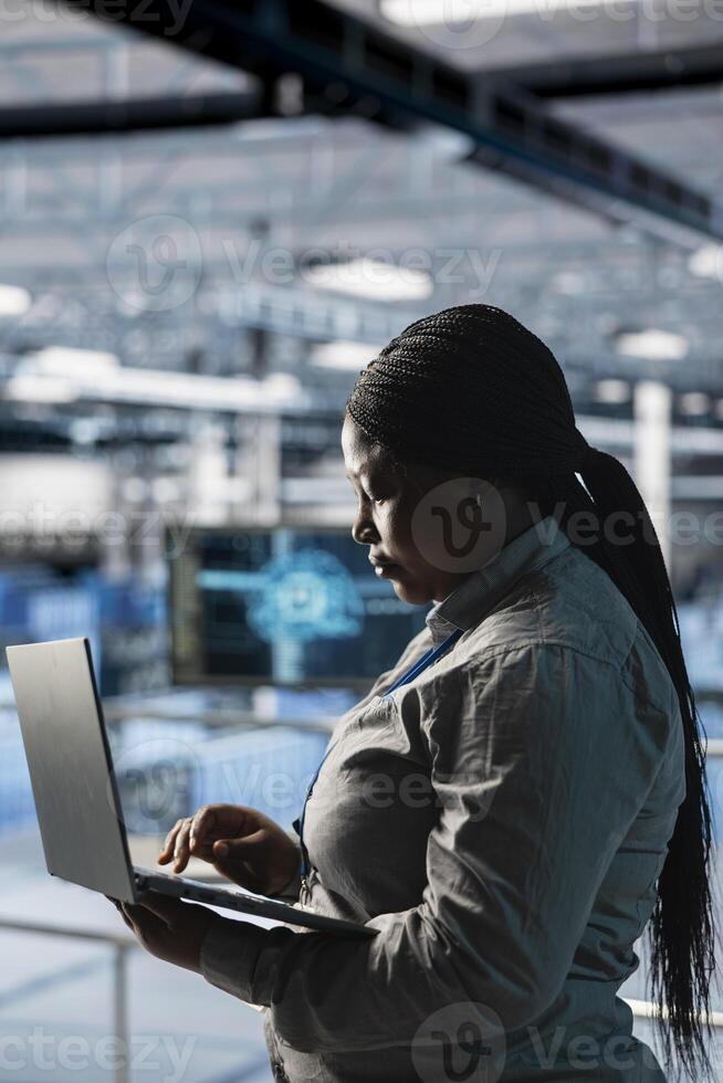 Female engineer in data center using laptop to configure hardware specifically optimized for AI tasks. Woman doing maintenance on rigs performing load balancing for artificial intelligence computing photo