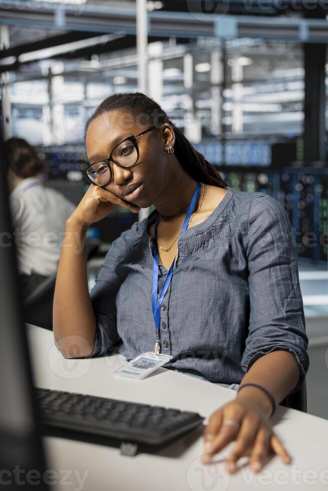 Exhausted server farm IT specialist strained after looking at computer screen for too long. Tired African american technician in data center stressed by long hardware troubleshooting session photo