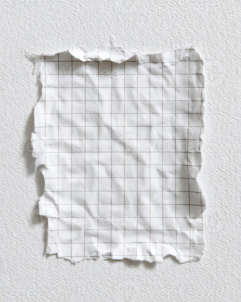 Torn, crinkled square of grid paper on a textured white surface, lit from above photo