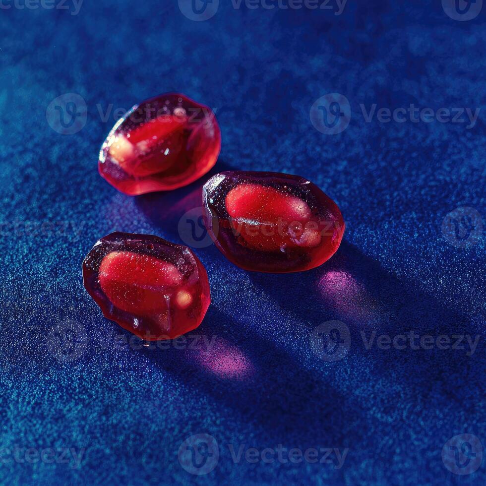 Three translucent ruby-red pomegranate seeds on a textured, deep blue surface, with light play photo