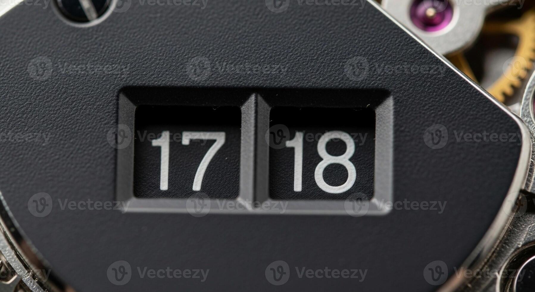 Close up view of a mechanical flip counter displaying the numbers seventeen and eighteen with intricate gears visible photo