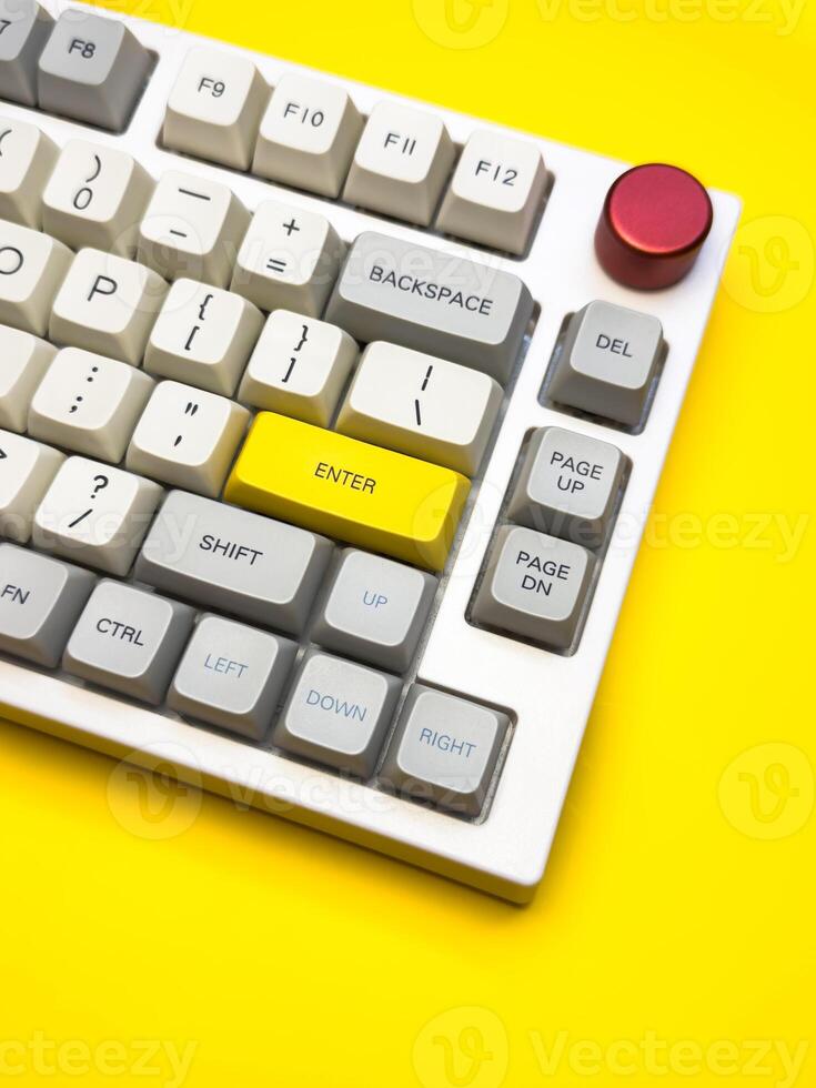 Vertical White mechanical keyboard with bright Enter key on bright yellow background, minimalism, keyboard buttons. A keyboard with a yellow key on the bottom left photo