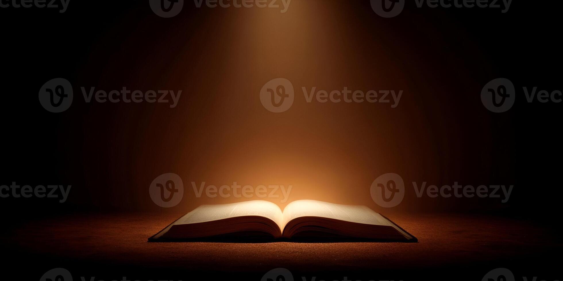 An old open book with glowing pages is illuminated by a ray of divine golden light in a dark mysterious setting photo