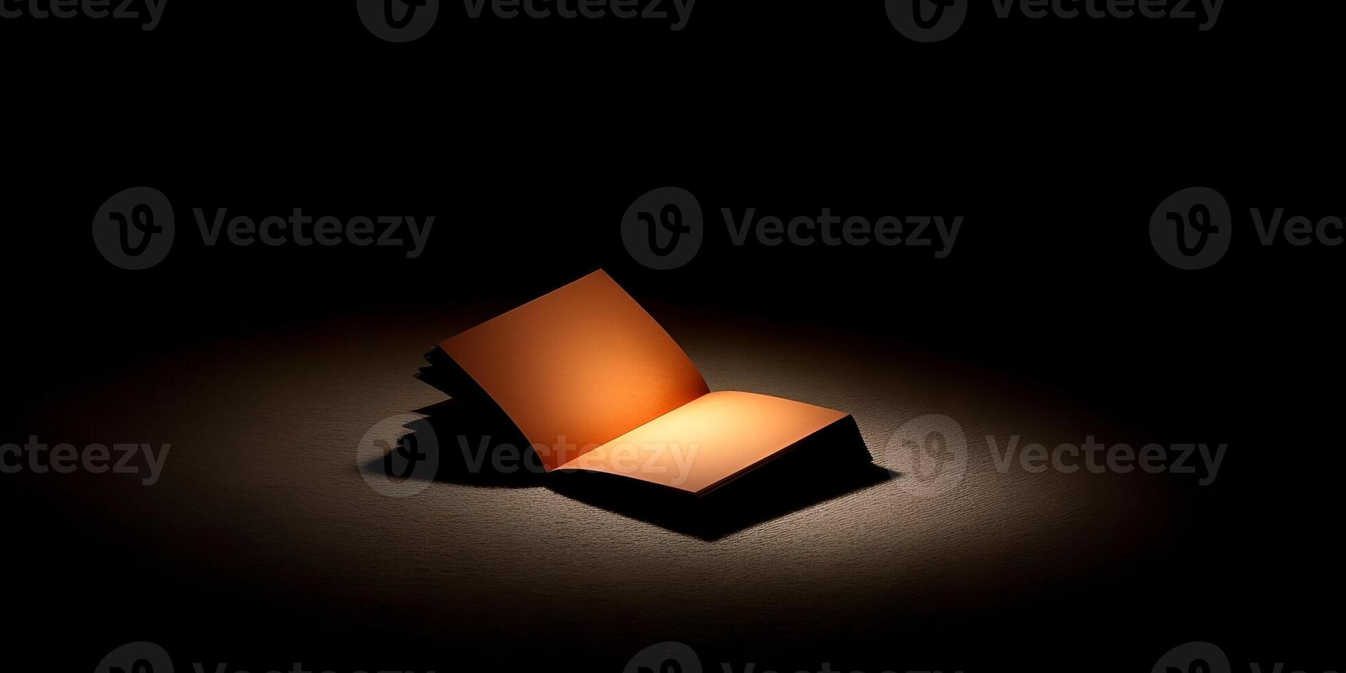 An open blank notebook is illuminated by a warm spotlight on a dark textured surface creating a dramatic and mysterious atmosphere photo