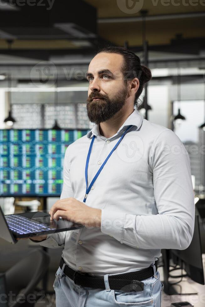 Corporate worker engaged in business analysis with laptop in hand, reviewing reports and charts using digital technology to enhance efficiency. Man aligning resources to achieve performance. photo