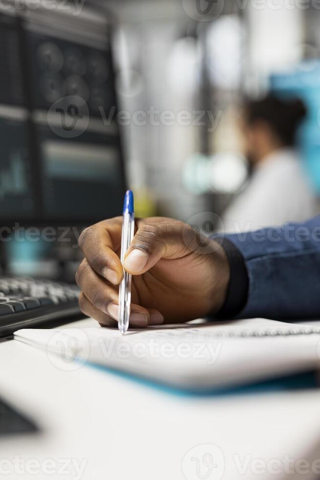 Close up of black business analyst takes notes on textbook in the office, examining charts and graphs to align company objectives with strategy. Drive progress and measurable performance. photo