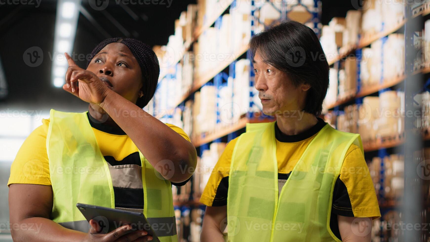 African american and asian team prepare shipments for dispatch with digital inventory and cargo pallets on depot racks. Working in a large scale distribution hub for express delivery. Camera B. photo