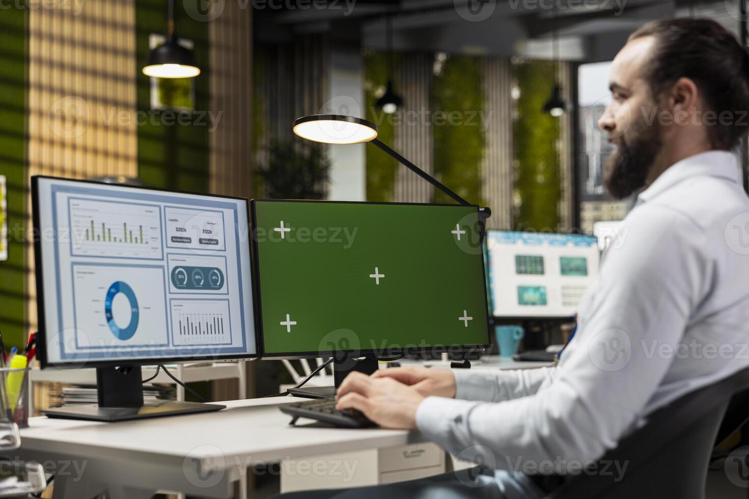 Young business analyst examining forecasts with chroma key on monitor, working on extracting performance metrics for a briefing. Boosting numbers for global expansion and networking. photo