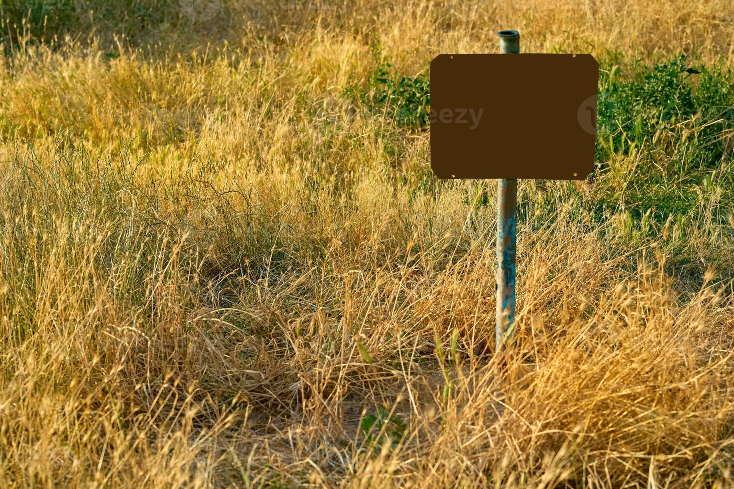 Rusty red frame for text on an old pipe in a field with dry grass photo