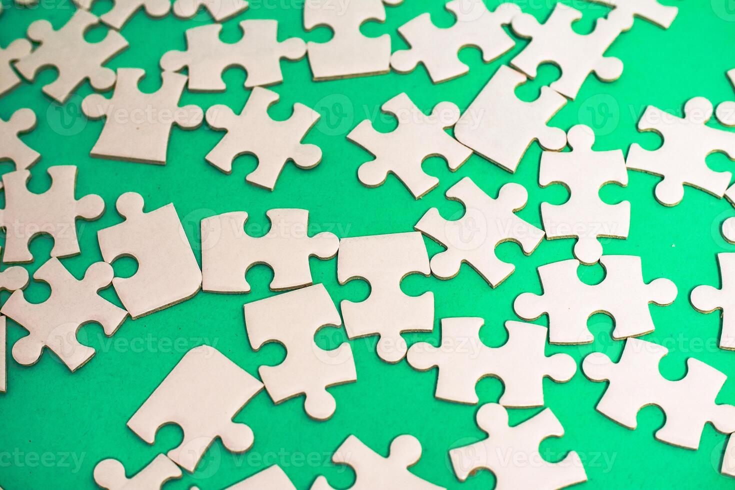 Scattered jigsaw puzzle pieces on a vibrant green background create a chaotic yet intriguing visual photo