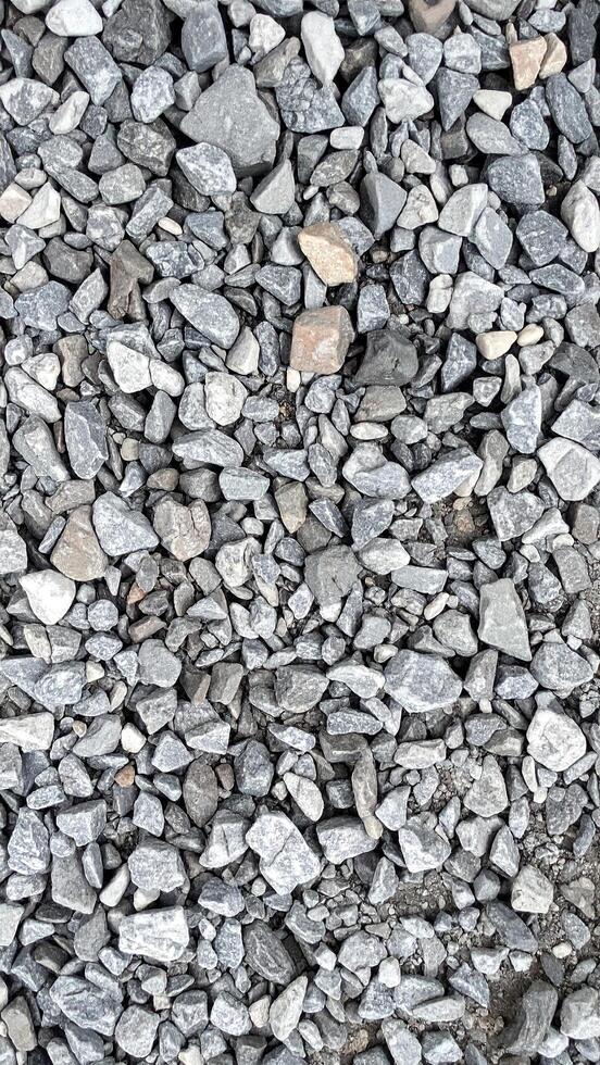 An overhead view of a dense pile of irregularly shaped, grey and dark rocks and pebbles, with some lighter beige stones scattered within, creating a textured, natural surface photo