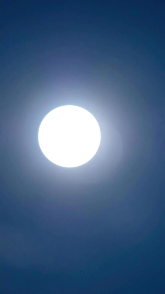 A bright, glowing sphere dominates a gradient blue sky. Light emanates outwards, causing a slight halo effect. The image is a simple, clean composition with a focus on illumination photo