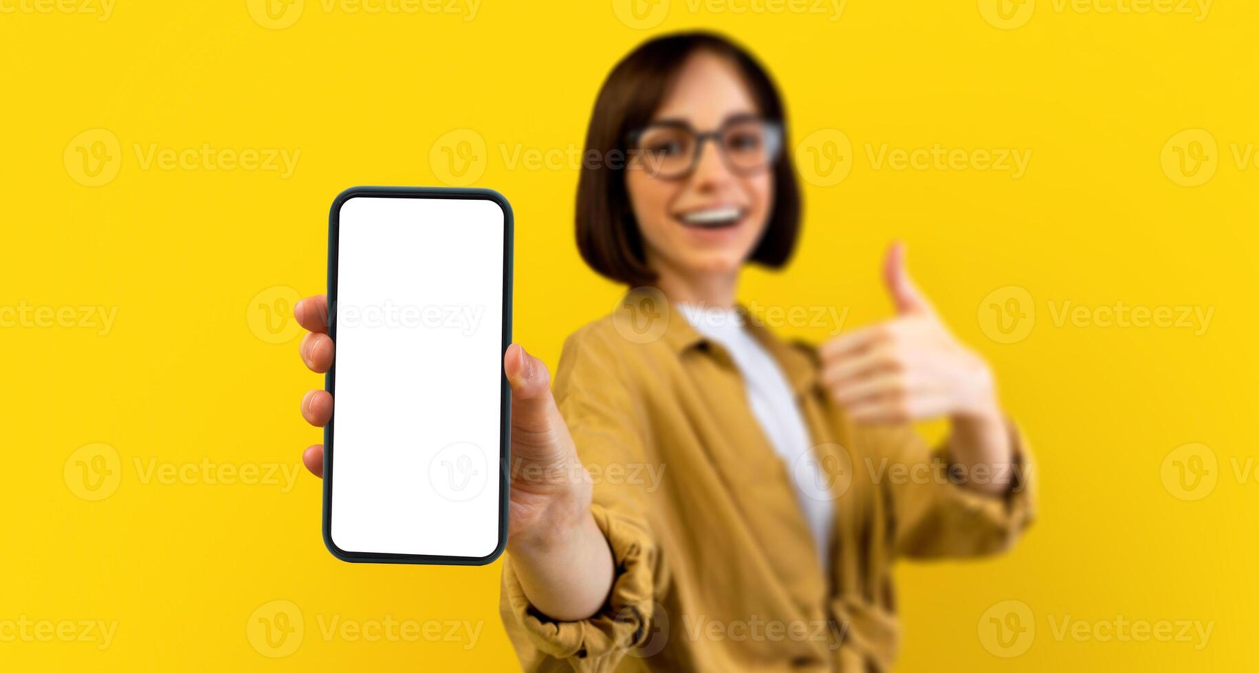 I recommend this app. Excited lady holding smartphone with black blank screen, showing device and thumb up gesture, standing over yellow background. Gadget with empty space for mockup photo