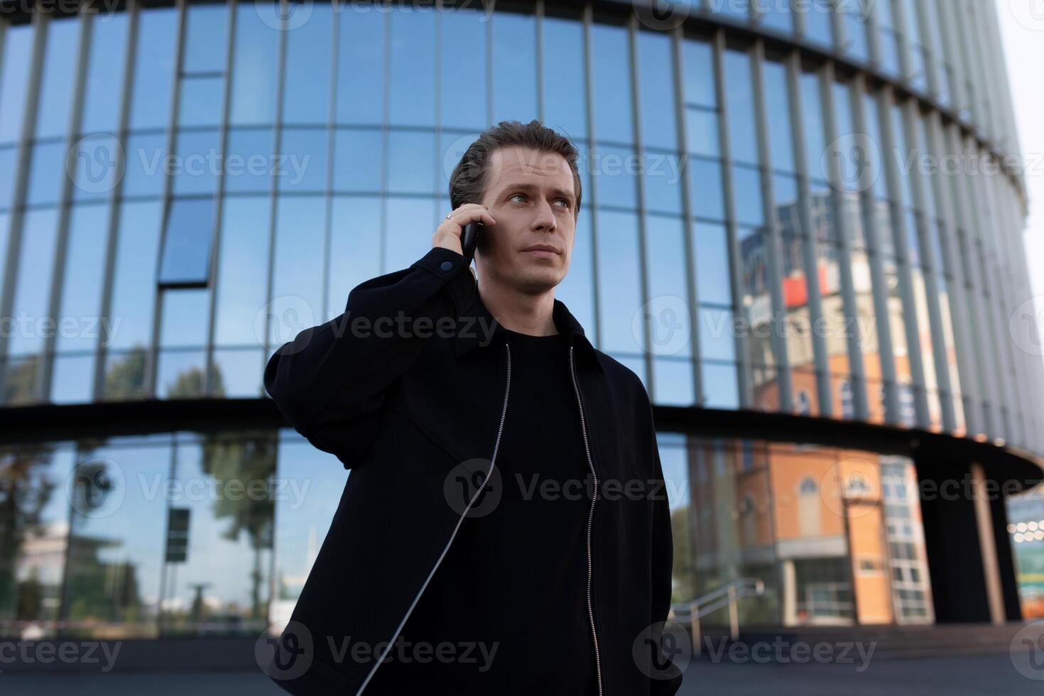 Man using smartphone while standing in front of modern glass building photo