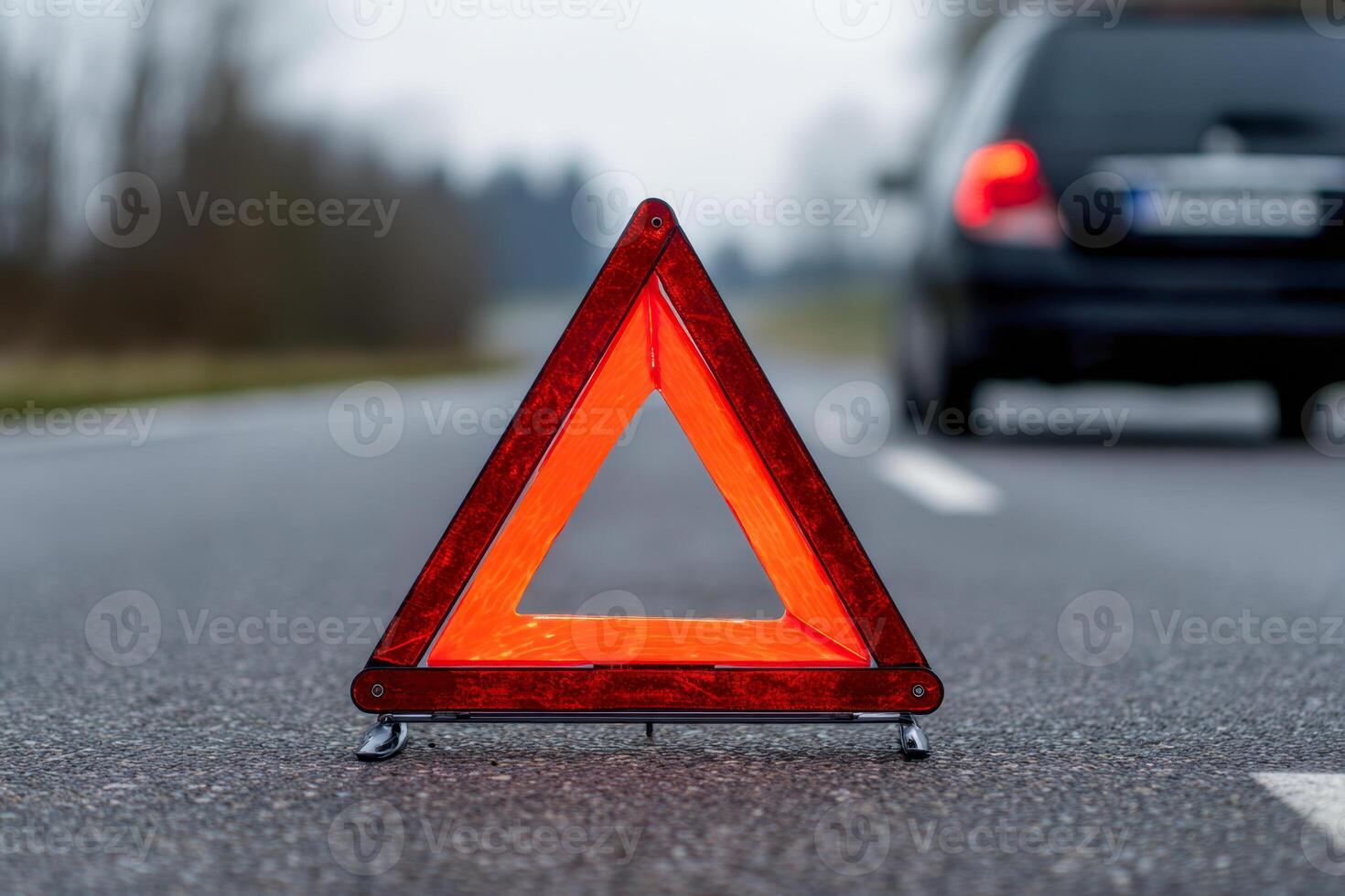 Red reflective warning triangle placed on an empty highway to signal a vehicle breakdown with a blurred car driving past in the background on a gloomy day photo