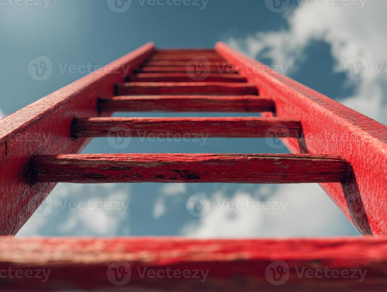 A close-up view of a vibrant red ladder reaching toward a partly cloudy sky, symbolizing aspiration, progress, and the pursuit of higher goals from a low-angle perspective. photo